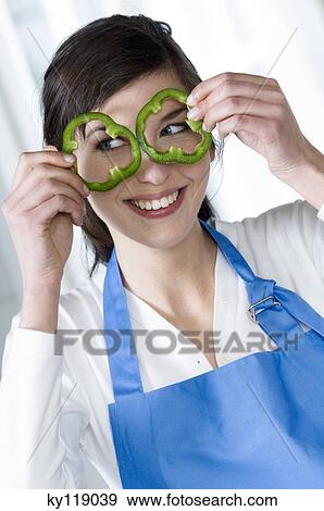Young smiling woman holding 2 green pepper slices in front of her eyes View Large Photo Image Stock Photo - Young smiling woman holding 2 green pepper slices in front of her eyes. Fotosearch