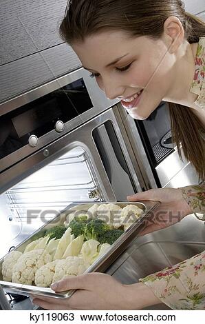 Young smiling woman putting broccolis and cauliflowers into an oven View Large Photo Image Stock Image - Young smiling woman putting broccolis and cauliflowers into an oven. Fotosearch
