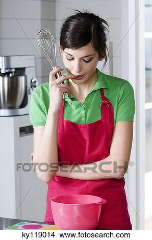 Young thinking woman in the kitchen, holding a whisk View Large Photo Image Picture - Young thinking woman in the kitchen, holding a whisk. Fotosearch
