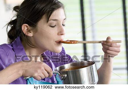Stock Image - Young woman tasting tomato sauce. Fotosearch
