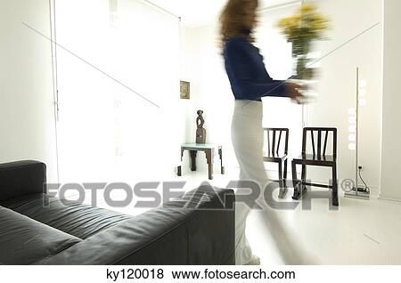 Woman carrying a vase of flowers in a living-room View Large Photo Image Stock Photo - Woman carrying a vase of flowers in a living-room. Fotosearch