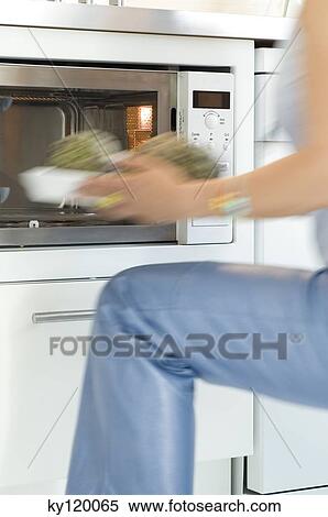 Stock Photography - Woman using a microwave, close-up. Fotosearch