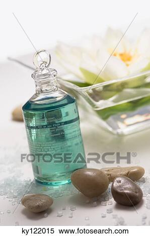 Stock Photography - Essential oil bottle, peebles and water lily flower, close-up. Fotosearch