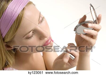 Stock Image - Portrait of a young woman making-up her mouth, indoors (studio). Fotosearch
