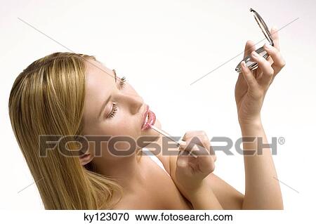 Stock Image - Portrait of a young woman making-up her mouth, indoors (studio). Fotosearch