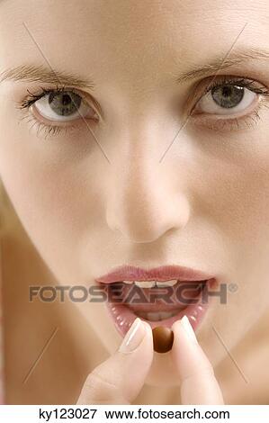 Portrait of a young woman opening her mouth for a brown tablet, indoors (studio) View Large Photo Image Stock Photo - Portrait of a young woman opening her mouth for a brown tablet, indoors (studio). Fotosearch