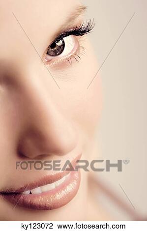 Stock Image - Portrait of a young woman smiling, looking at the camera, close-up of half of her face, indoors (studio). Fotosearch