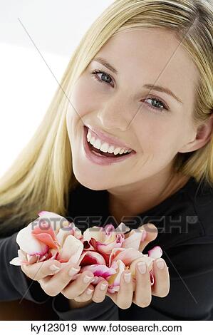 Stock Photo - Portrait of a young woman smiling, holding flowers petals, indoors (studio). Fotosearch
