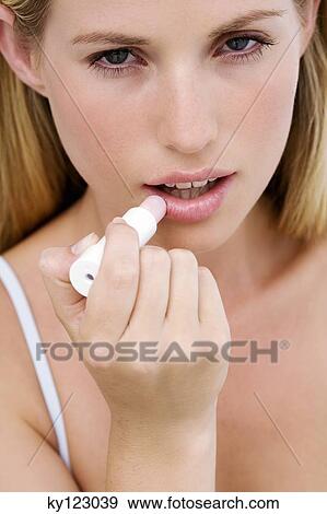 Stock Photo - Portrait of a young woman using a lip balm. Fotosearch
