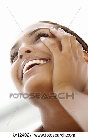 Stock Photo - Portrait of a young smiling woman, looking up, hand on cheek. Fotosearch