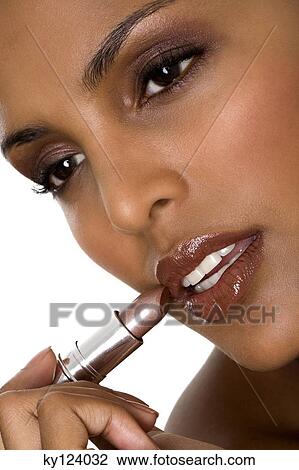 Stock Image - Portrait of a young woman applying lipstick. Fotosearch