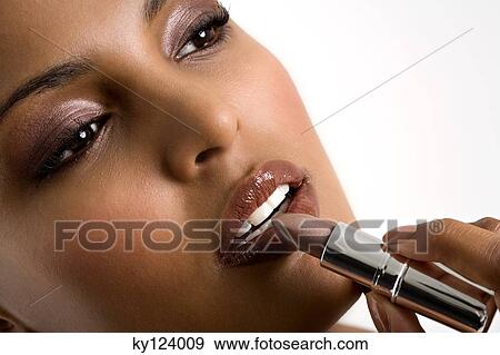 Portrait of a young woman applying lipstick View Large Photo Image Stock Photo - Portrait of a young woman applying lipstick. Fotosearch