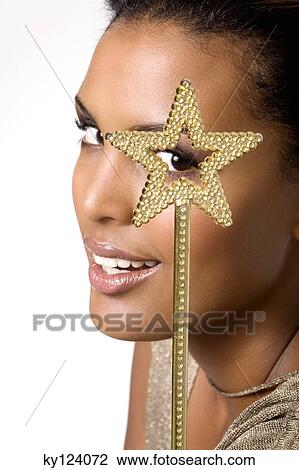 Stock Image - Portrait of a young woman looking through magic wand. Fotosearch