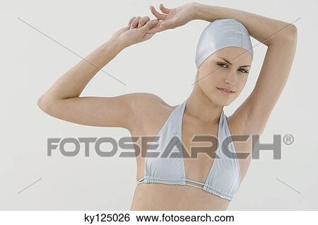 Stock Photograph - Portrait of a young woman with bikini and swimming cap, arms raised. Fotosearch