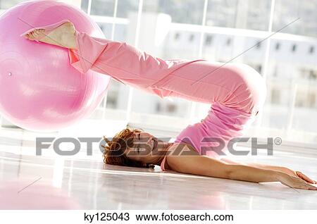 Stock Image - Young smiling woman lying on back, holding big pink balloon with feet. Fotosearch