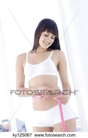 Stock Photo - Young smiling woman measuring waist with tape measure. Fotosearch