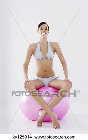 Picture - Young smiling woman, sitting on big pink balloon. Fotosearch