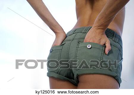 Stock Photograph - Young woman in shorts, hands in pocket, rear view. Fotosearch