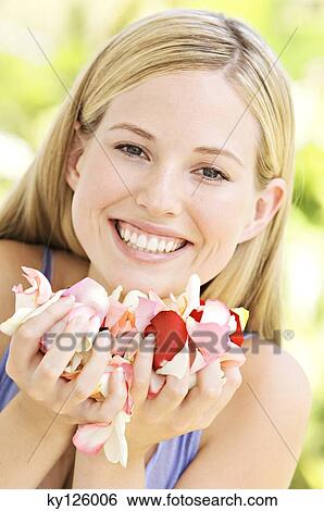 Stock Photograph - Portrait of a young blond woman smiling, holding petals, outdoors. Fotosearch