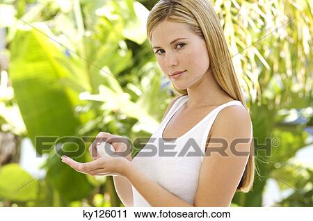 Stock Image - Portrait of a young woman applying moisturizer on her hand. Fotosearch