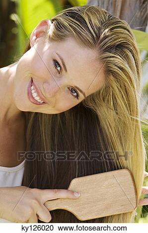 Stock Image - Portrait of a young woman brushing her hair, outdoors. Fotosearch