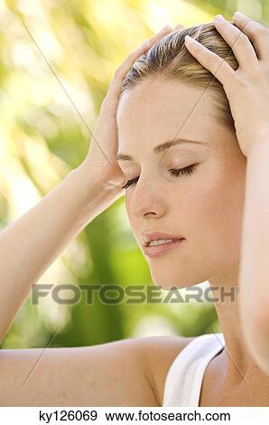 Stock Photo - Portrait of a young woman, eyes shut, hands on her head, outdoors. Fotosearch