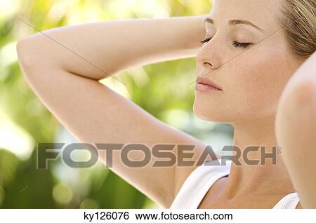 Stock Photograph - Portrait of a young woman, eyes shut, hands on her head, outdoors. Fotosearch