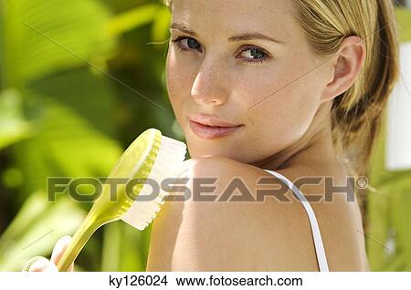 Portrait of a young woman looking at the camera, holding a brush agains her shoulder, outdoors View Large Photo Image Picture - Portrait of a young woman looking at the camera, holding a brush agains her shoulder, outdoors. Fotosearch