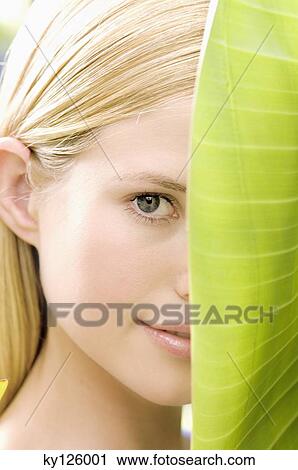 Stock Image - Portrait of a young woman looking at the camera, banana leaf, outdoors. Fotosearch