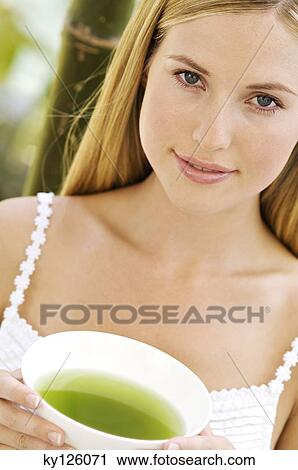 Portrait of a young woman looking at the camera, holding a green tea cup, outdoors View Large Photo Image Stock Image - Portrait of a young woman looking at the camera, holding a green tea cup, outdoors. Fotosearch