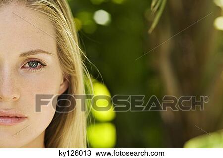 Stock Image - Portrait of half of a young woman's face, looking at the camera, close-up, outdoors. Fotosearch