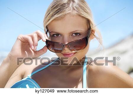Portrait of a young woman looking over her sunglasses View Large Photo Image Stock Photo - Portrait of a young woman looking over her sunglasses. Fotosearch