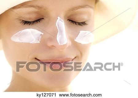 Stock Image - Portrait of a young woman with sun cream on face, eyes closed. Fotosearch