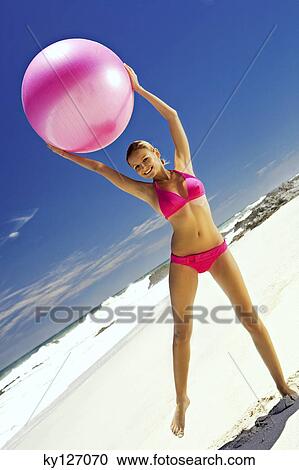 Young smiling woman in pink bikini on the beach, lifting a large ball View Large Photo Image Stock Image - Young smiling woman in pink bikini on the beach, lifting a large ball. Fotosearch
