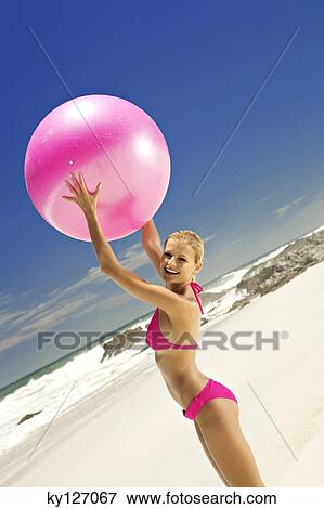 Young smiling woman in pink bikini on the beach, lifting a large ball View Large Photo Image Stock Photo - Young smiling woman in pink bikini on the beach, lifting a large ball. Fotosearch