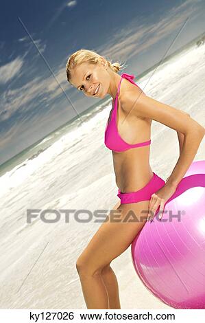 Young smiling woman in pink bikini on the beach, sitting on a large ball View Large Photo Image Stock Photograph - Young smiling woman in pink bikini on the beach, sitting on a large ball. Fotosearch