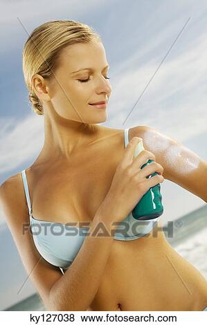 Stock Photo - Young woman in bikini, applying sun cream on her arm. Fotosearch