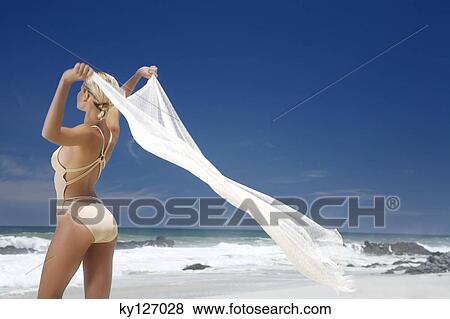 Stock Photo - Young woman in swimming costume holding white pareo in wind. Fotosearch