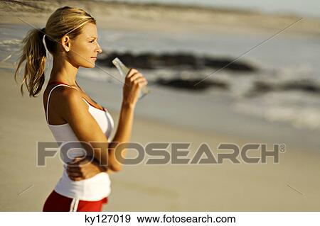 Stock Photo - Young woman standing on beach, drinking water from a bottle. Fotosearch