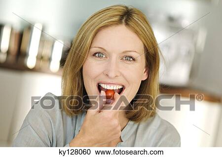 Stock Image - Portrait of a woman eating cherry tomato. Fotosearch