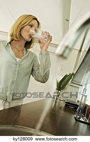 Woman drinking glass of water, tap in foreground View Large Photo Image Stock Photo - Woman drinking glass of water, tap in foreground. Fotosearch