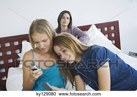 2 smiling teenage girls using mobile phones, woman in background View Large Photo Image Stock Image - 2 smiling teenage girls using mobile phones, woman in background. Fotosearch