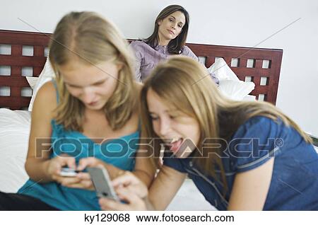 2 smiling teenage girls using mobile phones, woman in background View Large Photo Image Stock Photo - 2 smiling teenage girls using mobile phones, woman in background. Fotosearch