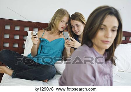 2 teenage girls sitting on bed, using mobile phones, thinking woman in foreground View Large Photo Image Stock Photo - 2 teenage girls sitting on bed, using mobile phones, thinking woman in foreground. Fotosearch