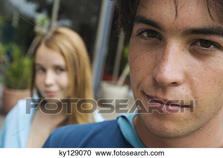 Stock Image - Portrait of a teenage boy looking at the camera, teenage girl in background. Fotosearch