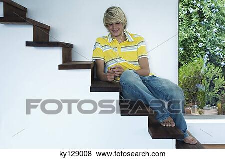Stock Photo - Teenage boy listening to music, sitting on stairs. Fotosearch