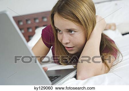 Teenage girl lying on bed, using laptop View Large Photo Image Stock Image - Teenage girl lying on bed, using laptop. Fotosearch