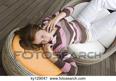 Teenage girl lying on chairs, using mobile phone View Large Photo Image Stock Photo - Teenage girl lying on chairs, using mobile phone. Fotosearch
