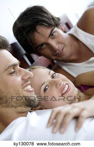 Stock Photo - 2 smiling men and a woman lying in bed. Fotosearch