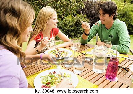 Stock Photo - 2 women and a man sitting at garden table. Fotosearch